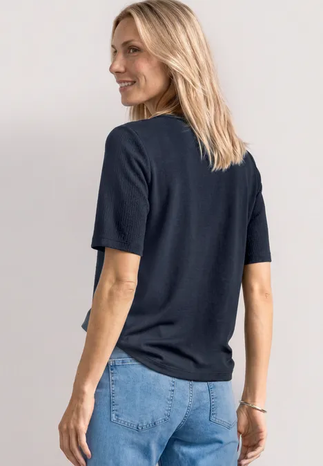 T-shirt à col rond avec boutons darkest blue Femme aux cheveux blonds vue de dos, portant un t-shirt noir et un jean bleu.