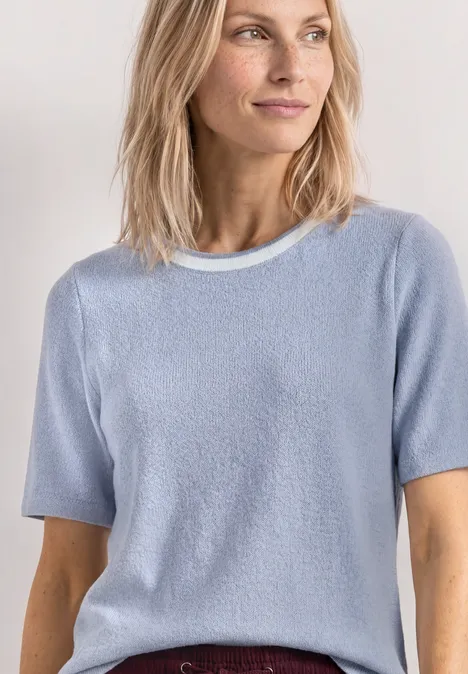 Shirt met gebreide look en ronde hals whispery blue Vrouw in lichtblauw T-shirt met korte mouwen en bordeauxrode rok voor lichte achtergrond.