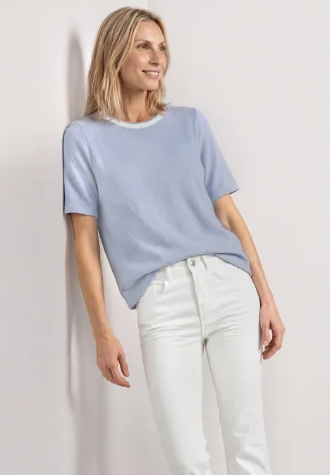 T-Shirt im Strick-Look mit Rundhals whispery blue Frau in hellblauem Kurzarmpullover und weißen Jeans vor hellem Hintergrund