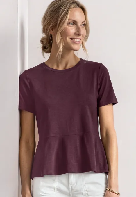 Shirt met ronde hals en volantdetail rustic rouge Vrouw in paars kort mouwshirt met uitlopende zoom en witte broek tegen een effen achtergrond.