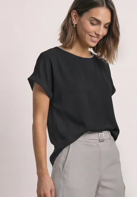 Femme en t-shirt noir décontracté et pantalon gris clair, style moderne et épuré.