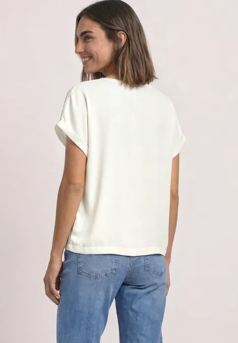 Une femme en t-shirt blanc et jean bleu regarde par-dessus son épaule et sourit.