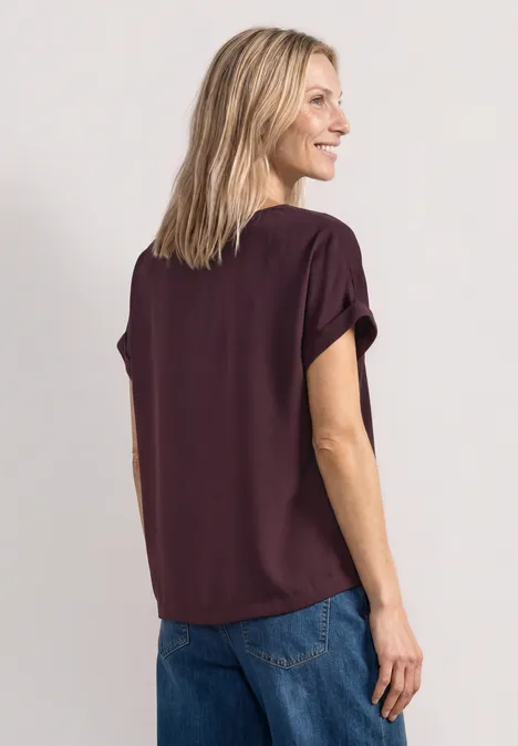 Femme vue de dos portant un chemisier violet et un jean, souriante, regard de côté.