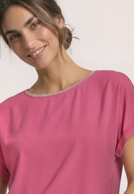 Eine lächelnde Frau in einem pinken Oberteil vor hellem Hintergrund.