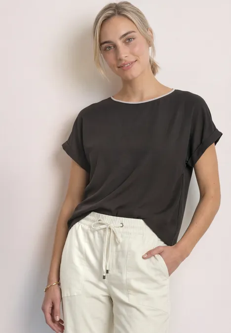 T-shirt 2 en 1 en chiffon, col bateau black coffee Une femme souriante porte un t-shirt noir et un pantalon beige décontracté, fond clair.