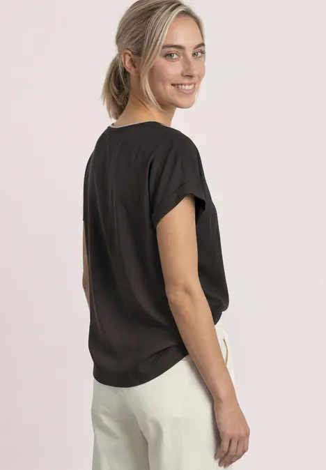 T-shirt 2 en 1 en chiffon, col bateau black coffee Une femme en chemisier noir et pantalon blanc, tournée et souriant par-dessus son épaule.