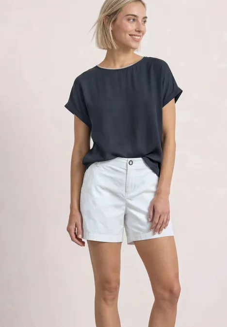 2-in-1 Shirt aus Chiffon mit Boat Neck darkest blue Eine Frau in marineblauem T-Shirt und weißen Shorts vor hellem Hintergrund.