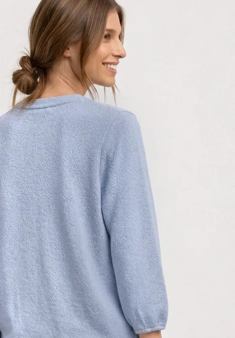 Eine Frau im hellblauen Strickpullover mit langen Ärmeln, Rücken zur Kamera gewandt.
