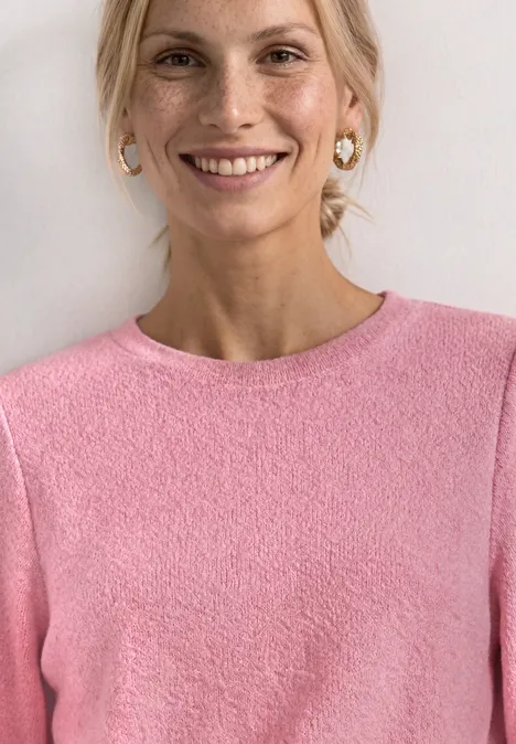 Pull en maille à manches 3/4 et col rond blush berry mel. Nahaufnahme einer Person in rosa Pullover mit goldenen Ohrringen, Gesicht unscharf