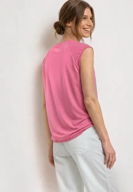 Dropped Shoulder Shirt mit Elastiksaum blush berry Eine Frau steht seitlich vor weißer Wand, trägt ärmelloses pinkes Top und weiße Hose.