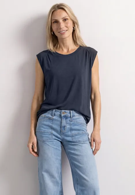 Blonde Frau in ärmellosem Dunkelblauem Top und lockerer hellblauer Jeans, legerer Look.