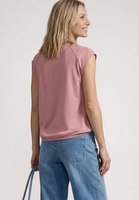 Rückansicht einer Frau in rosa Top und blauer Jeans, die eine Tasche in der Hand hält.