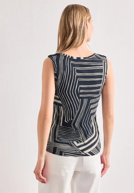 Haut à col en V et boutons décoratifs darkest blue Frau von hinten in ärmellosem Oberteil mit schwarz-weißen geometrischen Streifen vor weißer Wand.