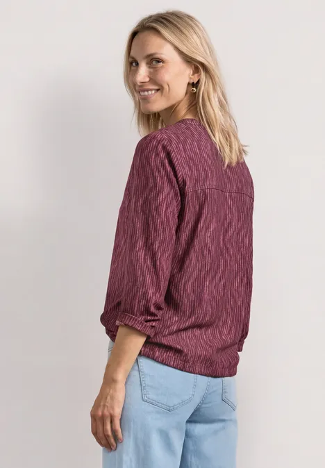 Frau mit lila Pullover und Jeans, steht seitlich, Blick vom Betrachter weg
