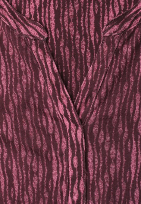 Dunkelrotes Oberteil mit pinkfarbenen, unregelmäßigen Wellenstreifen und V-Ausschnitt.