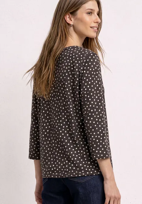 3/4-Arm Shirt mit Split Neck und Print black coffee Frau von hinten mit schwarzem, weiß gepunktetem 3/4-Arm-Shirt und Jeans, schaut seitlich lächelnd.