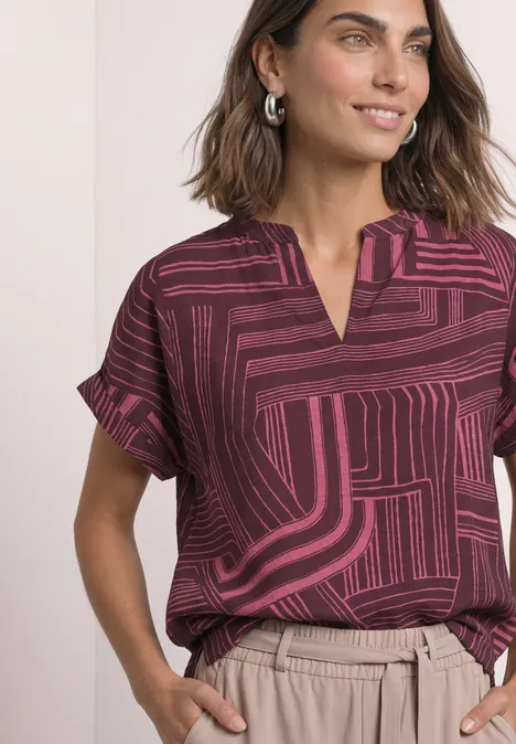 Dropped Shoulder Shirt mit Split Neck blush berry Frau trägt bordeauxrote, gemusterte Bluse mit V-Ausschnitt und beige Hose, silberne Creolen, lässiges Outfit.