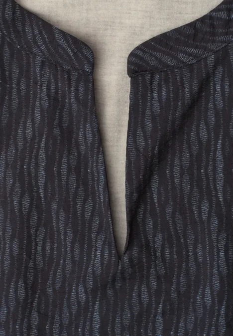T-shirt sombre à motifs ondulés bleus et col en V sur un fond de tissu clair.