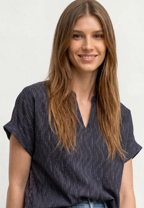 Souriante femme aux longs cheveux bruns portant un chemisier sombre à fines rayures.