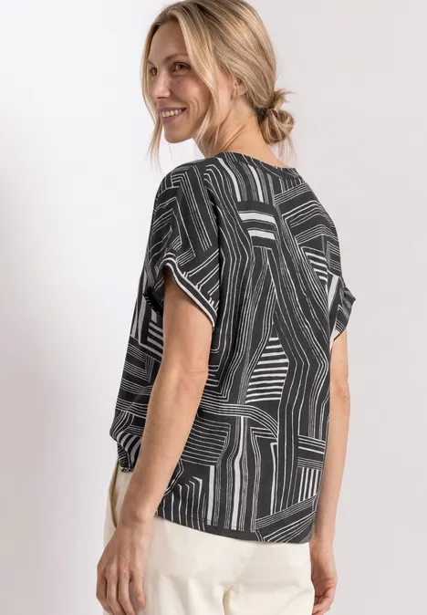 Une femme souriante en haut noir et blanc à motifs regarde par-dessus son épaule, pantalon clair.