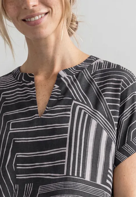 Femme en haut noir et blanc à motif géométrique, souriante, décolleté en V discret.