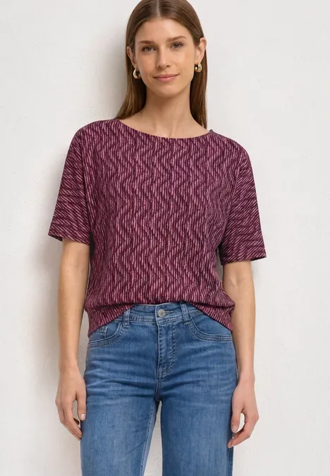 Frau trägt lila T-Shirt mit Wellenmuster und blaue Jeans.