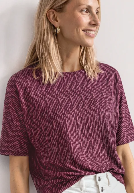 Shirt met boothals en elastische zoom blush berry Eine Person trägt ein kurzärmeliges, dunkelpinkes, gemustertes Shirt und weiße Hosen.