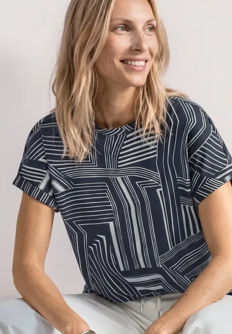 Frau trägt dunkelblaues T-Shirt mit weißem geometrischem Streifenmuster und kurzen Ärmeln, im Porträt.