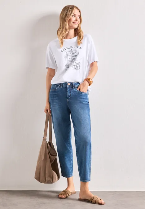 T-Shirt mit Rundhals und Frontprint White Frau in weißem Print-T-Shirt, hoch taillierten blauen Jeans, braunen Sandalen und großer Handtasche.