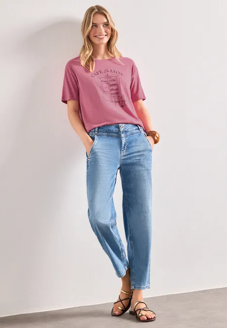 T-Shirt mit Rundhals und Frontprint blush berry Frau trägt rosa T-Shirt, lockere blaue Jeans und schwarze Sandalen, steht entspannt mit Händen in den Taschen.