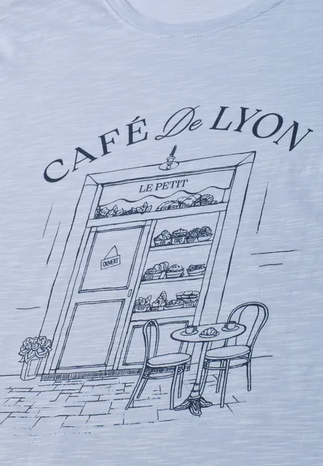 T-Shirt mit Rundhals und Frontprint whispery blue Zeichnung auf T-Shirt: Eingang des 'Café De Lyon' mit Auslage voller Gebäcke, Tisch und Stühlen.