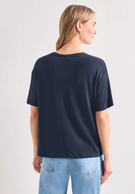 T-Shirt mit Rundhals und Frontprint darkest blue Frau steht mit dem Rücken zur Kamera, trägt dunkelblaues T-Shirt und helle Jeans vor weißer Wand.
