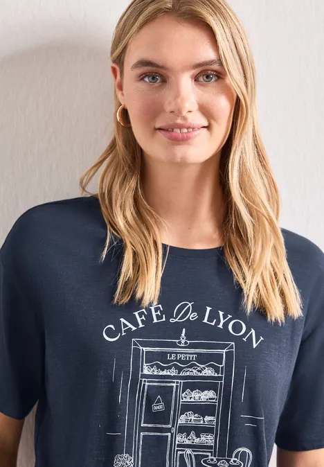 T-Shirt mit Rundhals und Frontprint darkest blue Frau mit blonden Haaren trägt ein navyblaues T-Shirt mit 'Café de Lyon' Aufdruck und einer skizzierten Bäckerei.