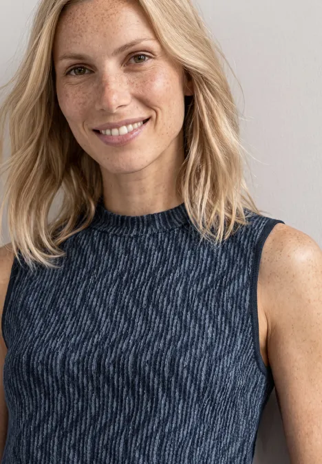 Porträt einer lächelnden, blondhaarigen Frau mit Sommersprossen in einem dunkelblauen, ärmellosen Top.