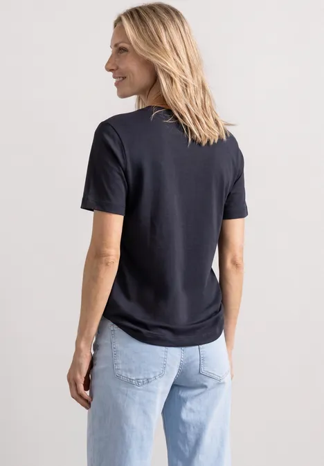 Rückansicht einer Frau in schwarzem T-Shirt und hellblauen Jeans, sie schaut lächelnd zur Seite.