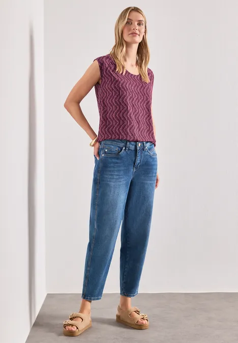 Femme devant un mur blanc portant un top en maille violet, jean ample et sandales à plateforme.