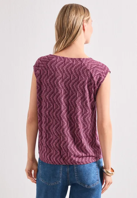 Femme vue de dos portant un haut violet à motif et un jean bleu.