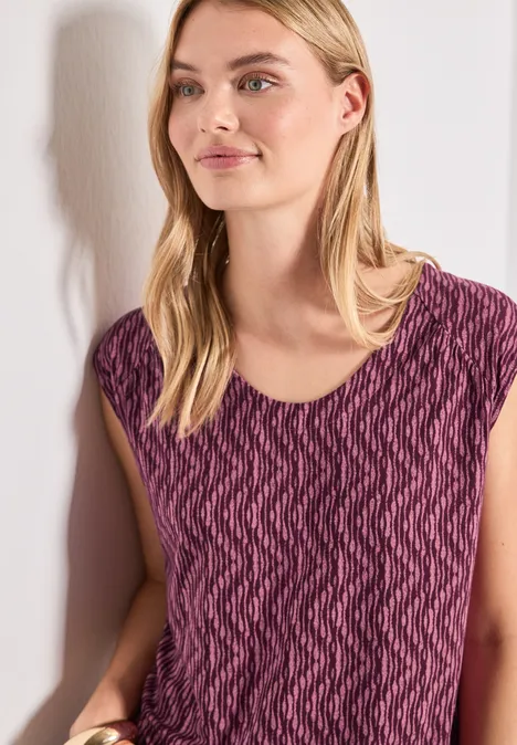 Femme appuyée sur mur blanc portant un haut violet à motif zigzag