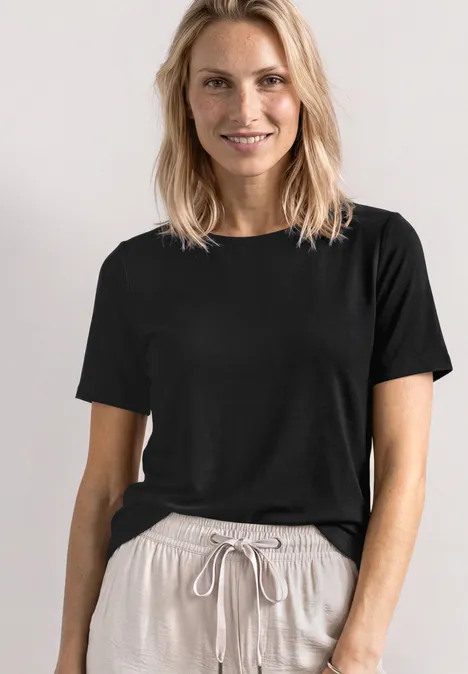 Basic Shirt met ronde hals in Unifarbe Black Een persoon draagt een effen zwart T-shirt en lichtbeige joggingbroek.