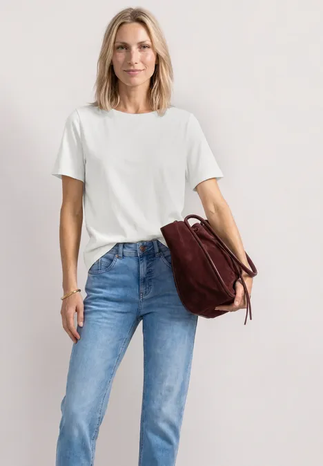Frau in weißem T-Shirt und blauen Jeans, lässig mit brauner Lederhandtasche.