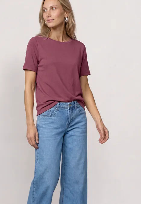 Eine Person trägt ein kurzärmeliges rosafarbenes T-Shirt und weite, hoch taillierte blaue Jeans.