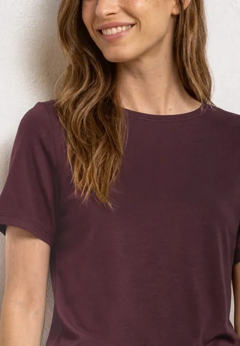 Eine Frau trägt ein schlichtes kurzärmeliges T-Shirt in dunklem Violett.