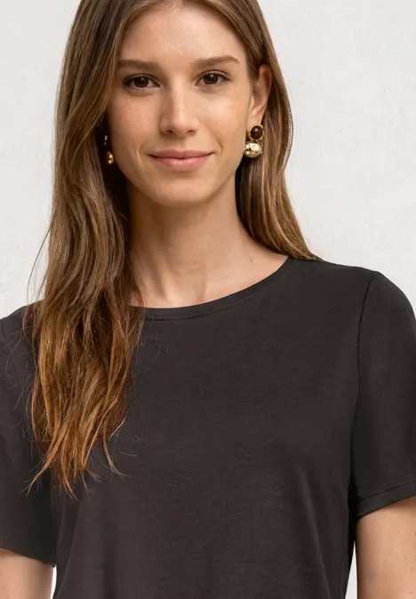 Junge Frau mit langem Haar trägt ein schlichtes dunkelgraues T-Shirt.