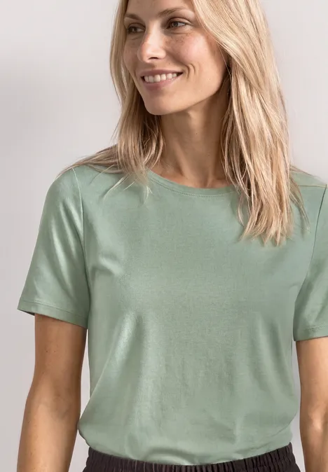 Frau mit langen blonden Haaren trägt schlichtes mintgrünes T-Shirt.