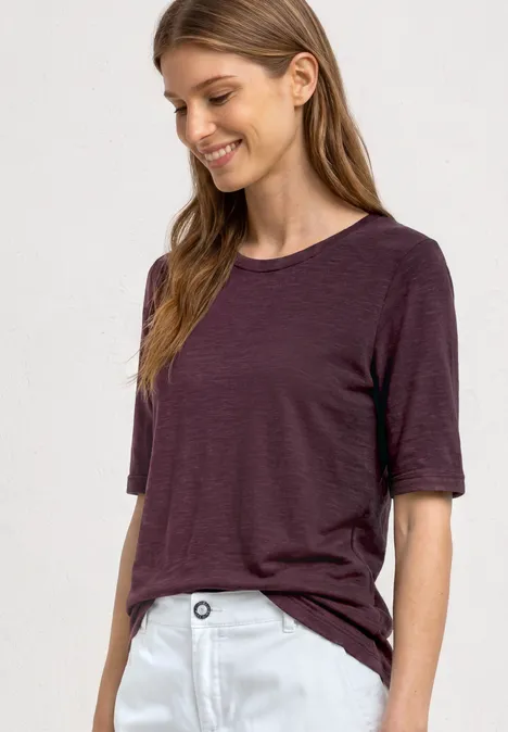 Basic Shirt met ronde hals in Unifarbe rustic rouge Jonge vrouw in los violet T-shirt met halve mouwen en witte broek voor een lichte achtergrond.