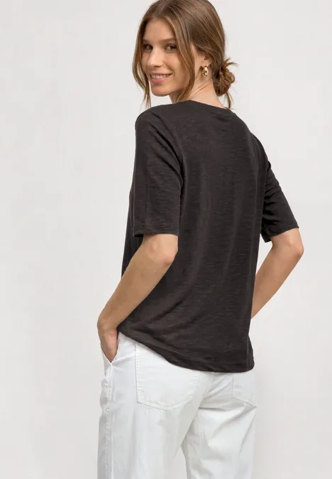Basic Shirt met ronde hals in Unifarbe black coffee Vrouw in donkergrijs T-shirt en witte broek kijkt glimlachend over haar schouder.