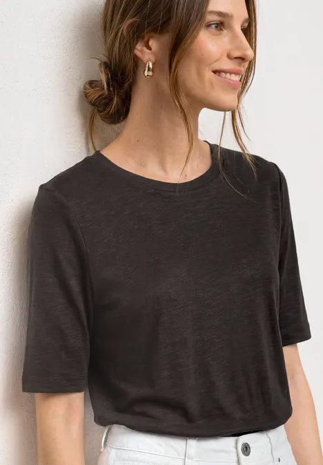 Basic Shirt met ronde hals in Unifarbe black coffee Vrouw in donkergrijs T-shirt met gouden oorbel en halsketting voor witte achtergrond