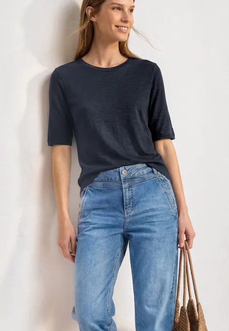 Basic Shirt met ronde hals in Unifarbe darkest blue Iemand draagt een donkerblauw T-shirt, een lichte spijkerbroek en houdt een gevlochten tas vast.
