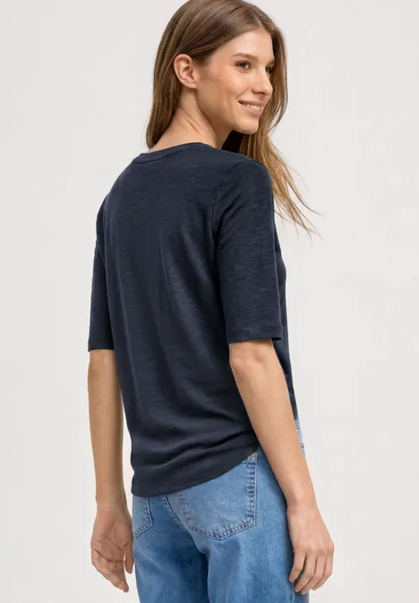 Basic Shirt met ronde hals in Unifarbe darkest blue Jonge vrouw in donker T-shirt en blauwe spijkerbroek kijkt over haar schouder.