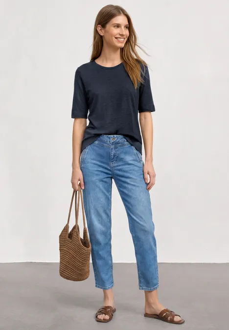 Basic Shirt met ronde hals in Unifarbe darkest blue Vrouw in blauw t-shirt, losse jeans en sandalen, met een bruine rieten tas voor een neutrale achtergrond.